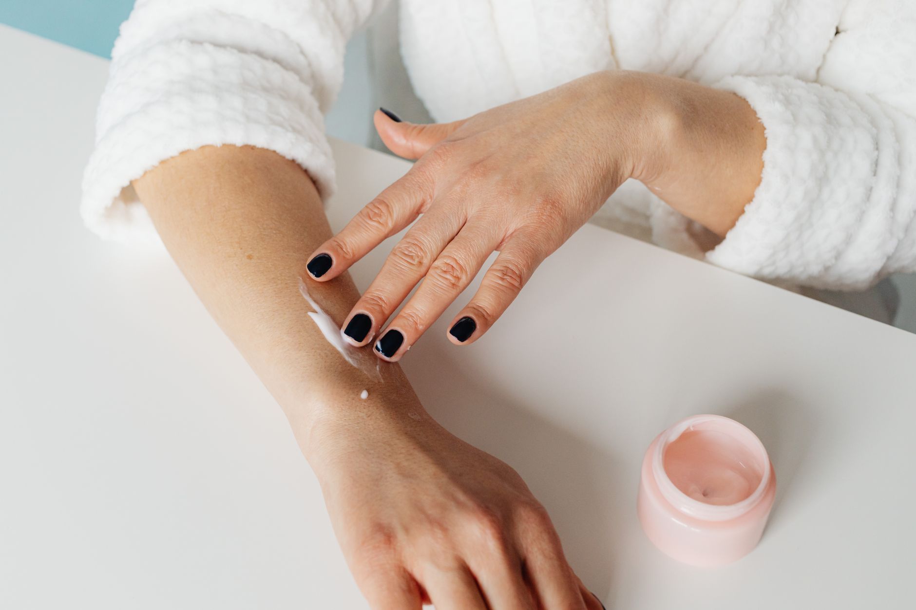 A woman rubbing cream into the back of her hand beside an open jar